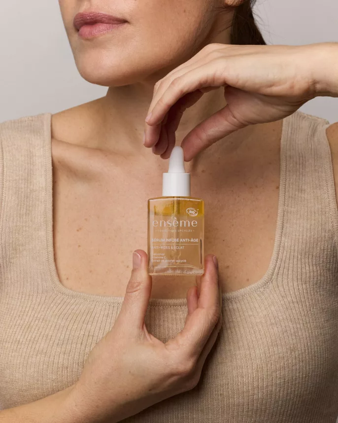 Gros plan sur un flacon de sérum anti-âge Ensème tenu par une femme, photographié sur fond neutre pour une campagne cosmétique à Lyon.