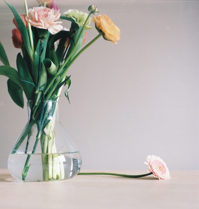 Vase de fleurs colorées avec une fleur tombée sur la table, photographie de Stéphanie Lorang, photographe à Lyon