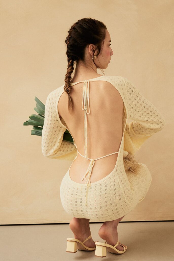 Portrait de dos d’une femme en robe ouverte, accroupie, tenant des poireaux