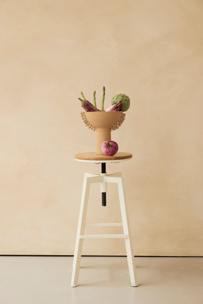 Photographie lifestyle d’une coupe design remplie de légumes, posée sur un tabouret minimaliste