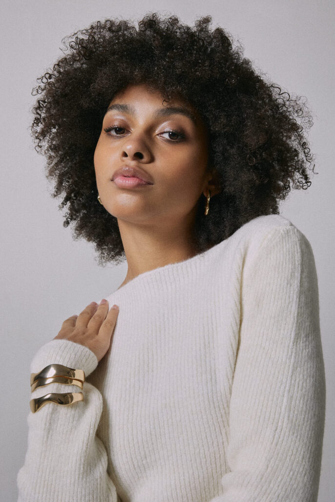 Portrait mode d’une femme au pull crème et bijoux dorés, capturé en studio par un photographe professionnel à Lyon — mise en valeur de la texture du vêtement et du bijou.