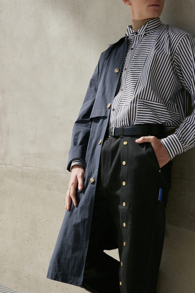 Photographie de mode homme à Lyon — mise en valeur des détails d’un look contemporain avec trench, chemise rayée et pantalon à boutons dorés, par Stéphanie Lorang, photographe de mode en région lyonnaise.