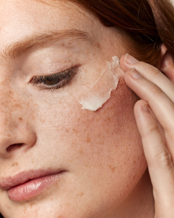 Portrait beauté en studio avec une modèle appliquant le baume nettoyant sur sa joue.