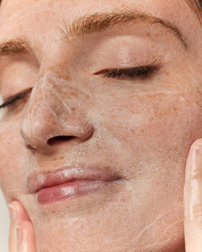 Portrait serré en studio montrant une modèle appliquant le baume nettoyant sur son visage, avec une mise en avant de la texture en action.