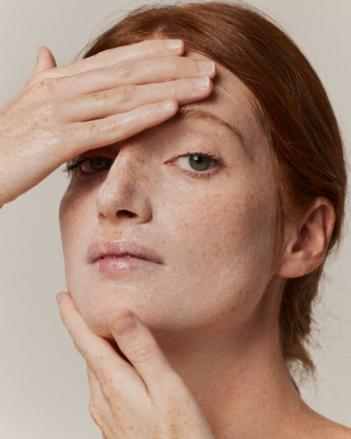 Portrait en studio d’une modèle appliquant un baume nettoyant sur son visage, avec un cadrage large