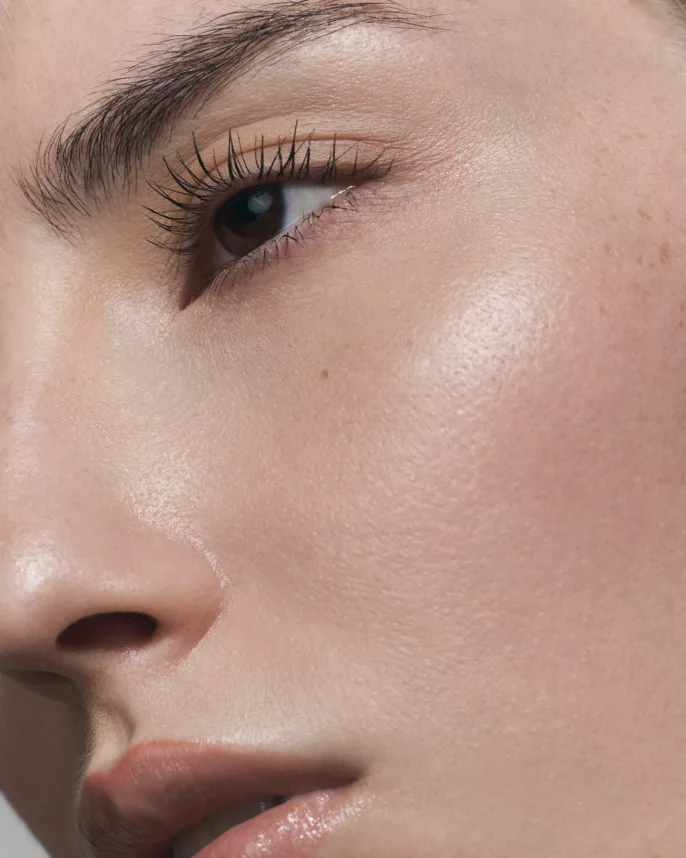 Gros plan sur un visage féminin avec peau nue lumineuse, regard intense et maquillage naturel.