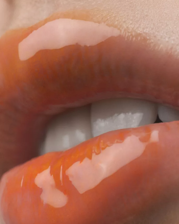 Macro d’une bouche maquillée avec un gloss orange brillant.