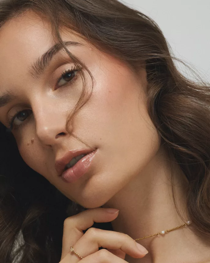 Portrait rapproché d’une femme portant un collier doré à perles et un maquillage lumineux.