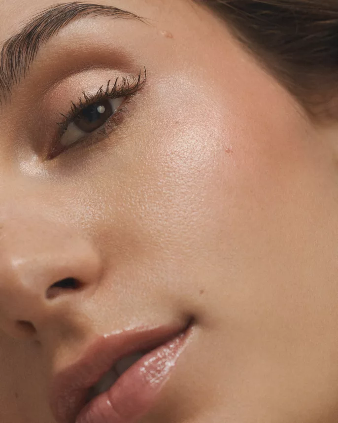 Gros plan sur le visage d’une femme avec un maquillage nude, peau lumineuse et lèvres brillantes.