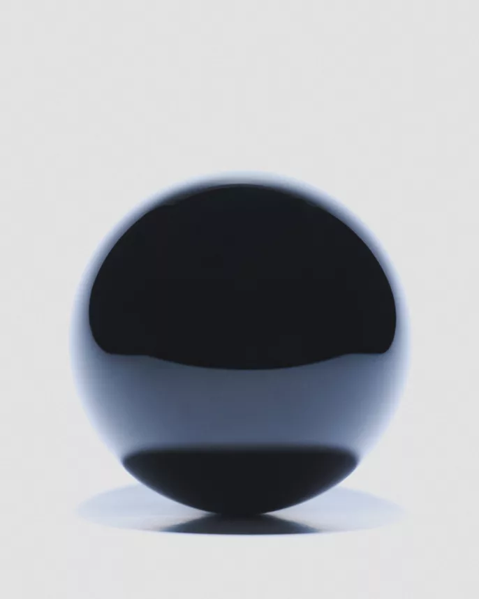 Photo studio d’une sphère noire brillante sur fond clair, mise en lumière minimaliste.