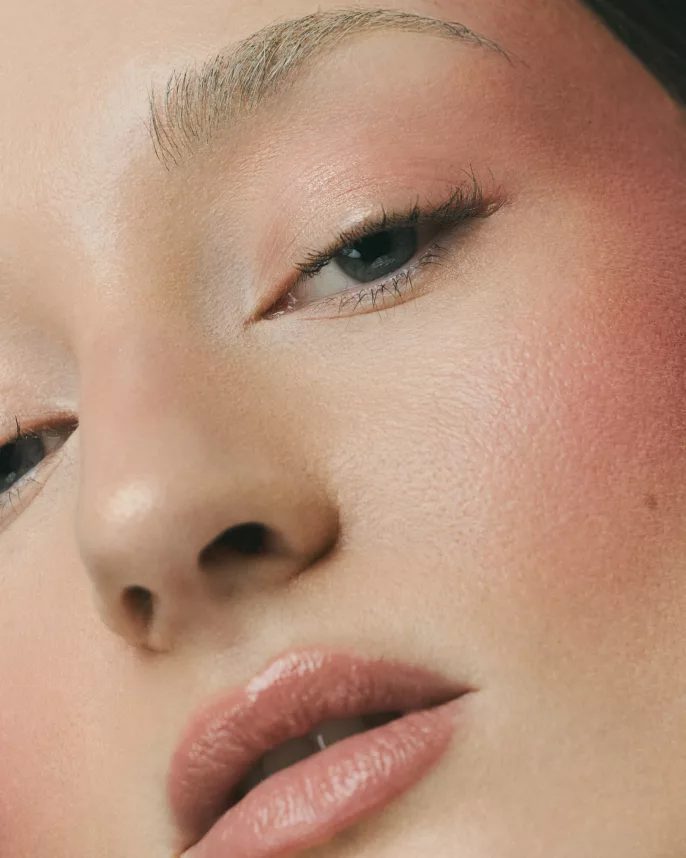 Gros plan maquillage sur visage féminin avec peau lumineuse et blush rosé, photographie beauté en studio.