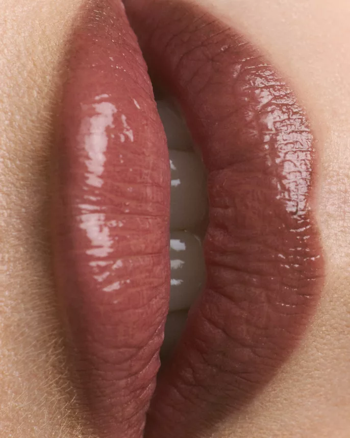 Gros plan de lèvres maquillées avec un rouge à lèvres brun glossy – photographie beauté en studio.