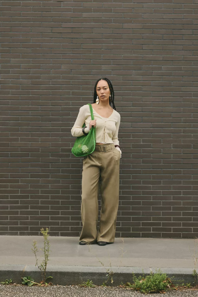 Modèle debout en tenue neutre avec sac vert devant un mur de briques – Photographe mode à Lyon