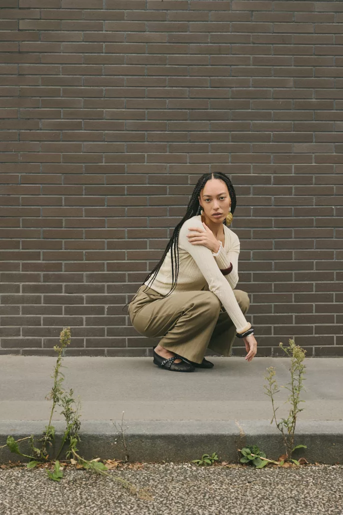 Modèle accroupie en tenue neutre devant un mur en briques – Photographe mode à Lyon