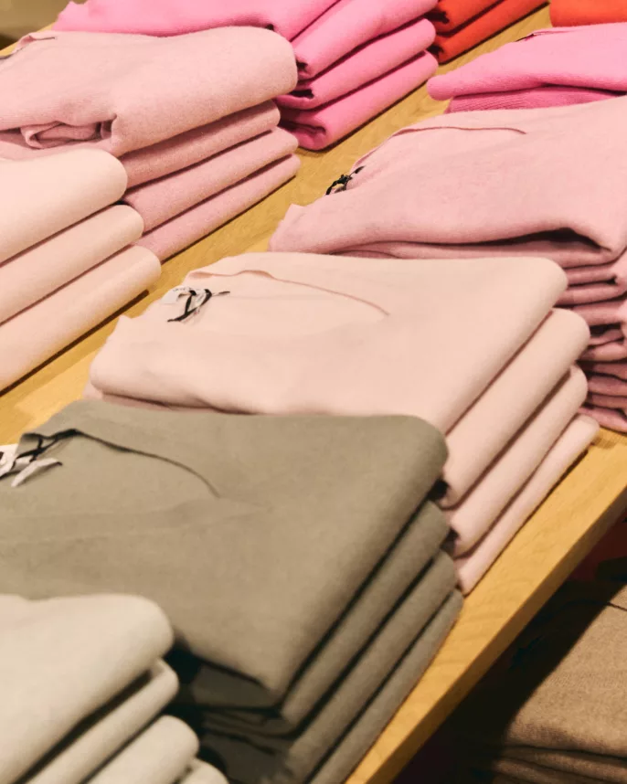 Reportage boutique prêt-à-porter – piles de pulls pliés par couleur sur table en magasin