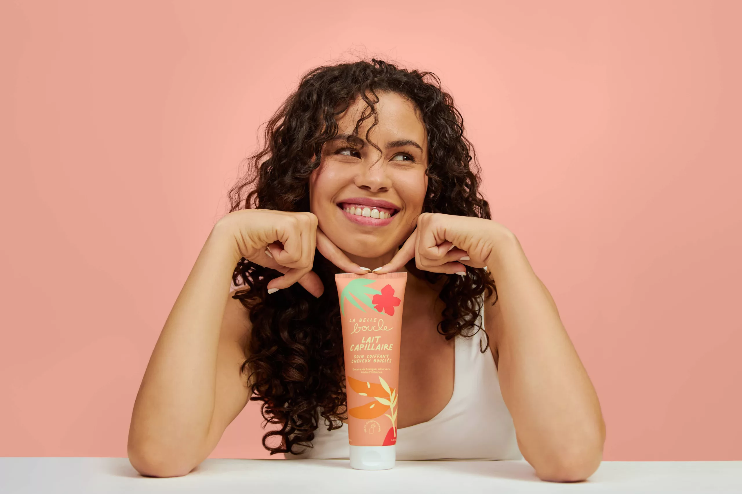 Modèle aux cheveux bouclés souriante, regard vers le haut, avec le lait capillaire La Belle Boucle — shooting beauté Lyon, Stéphanie Lorang