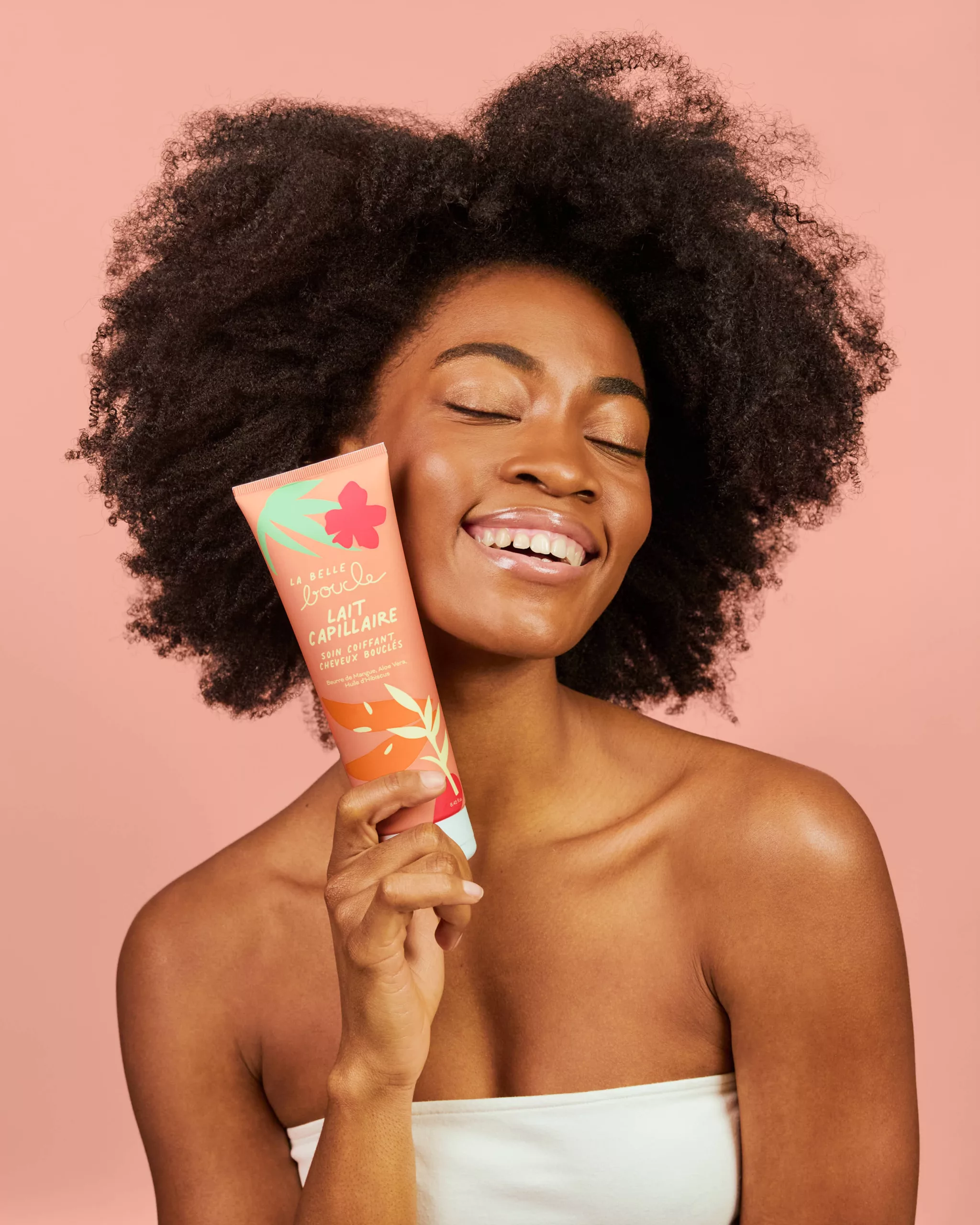 Modèle aux cheveux afro souriante, yeux fermés, tenant le lait capillaire La Belle Boucle — portrait beauté Lyon, Stéphanie Lorang