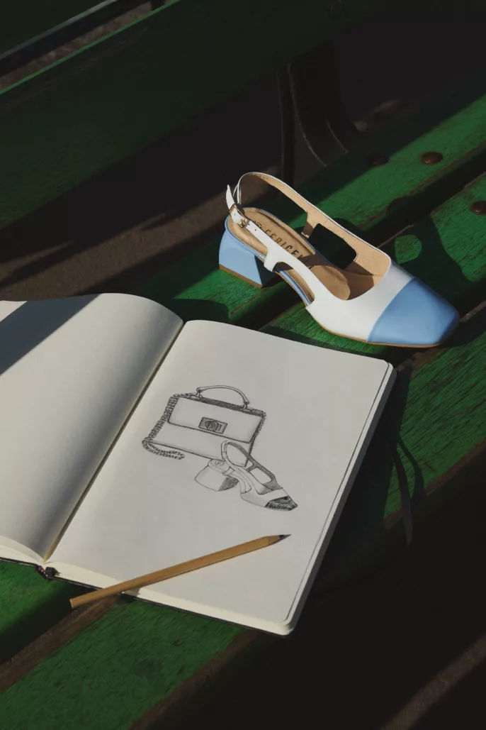 Photographie lookbook chaussures – escarpin bicolore posé sur banc avec carnet de croquis en extérieur
