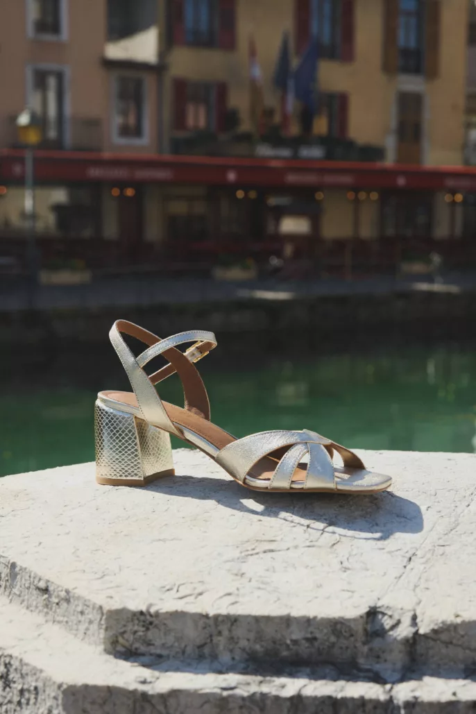 Photographie lookbook chaussures – sandale dorée posée sur pierre avec canal en arrière-plan