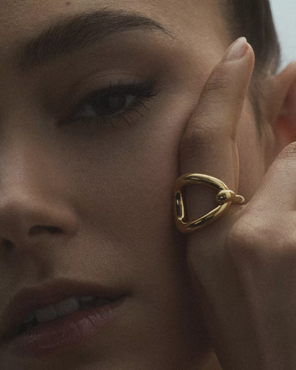 Gros plan sur bague dorée à forme organique portée sur fond de visage flou — photographie bijoux macro Lyon, Stéphanie Lorang