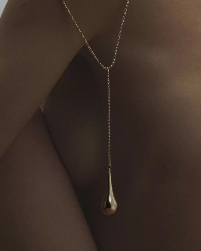 Collier sautoir doré à pendentif goutte sur peau sombre, lumière sculptante — photographie bijoux studio Lyon, Stéphanie Lorang