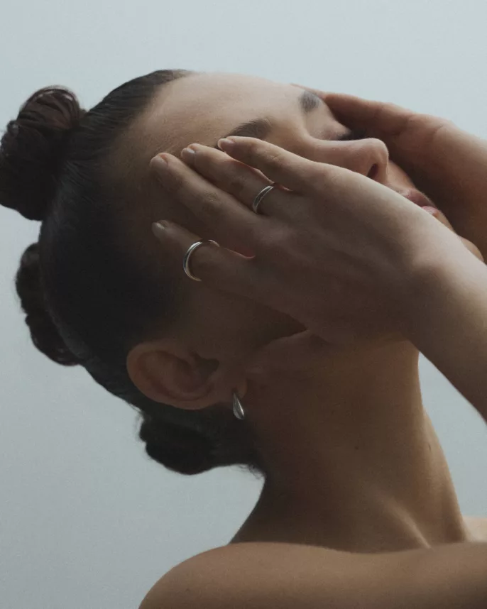 Modèle aux mains jointes sur le visage portant bagues et créoles argent — photographe bijoux Lyon, Stéphanie Lorang