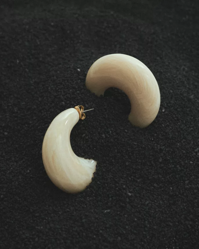 Créoles volumineuses en résine ivoire posées sur fond de graines noires — photographie bijoux studio Lyon, Stéphanie Lorang