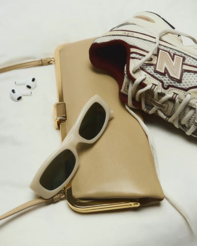 Sneaker New Balance, sac camel, lunettes crème et AirPods sur tissu blanc froissé — photographie éditoriale studio Lyon, Stéphanie Lorang